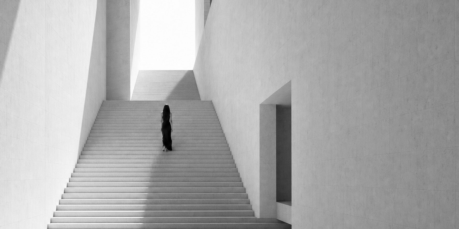 Eine Frau geht eine weiße Treppe hinauf ins Licht