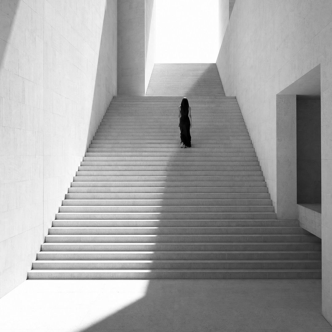 Eine Frau geht eine weiße Treppe hinauf ins Licht